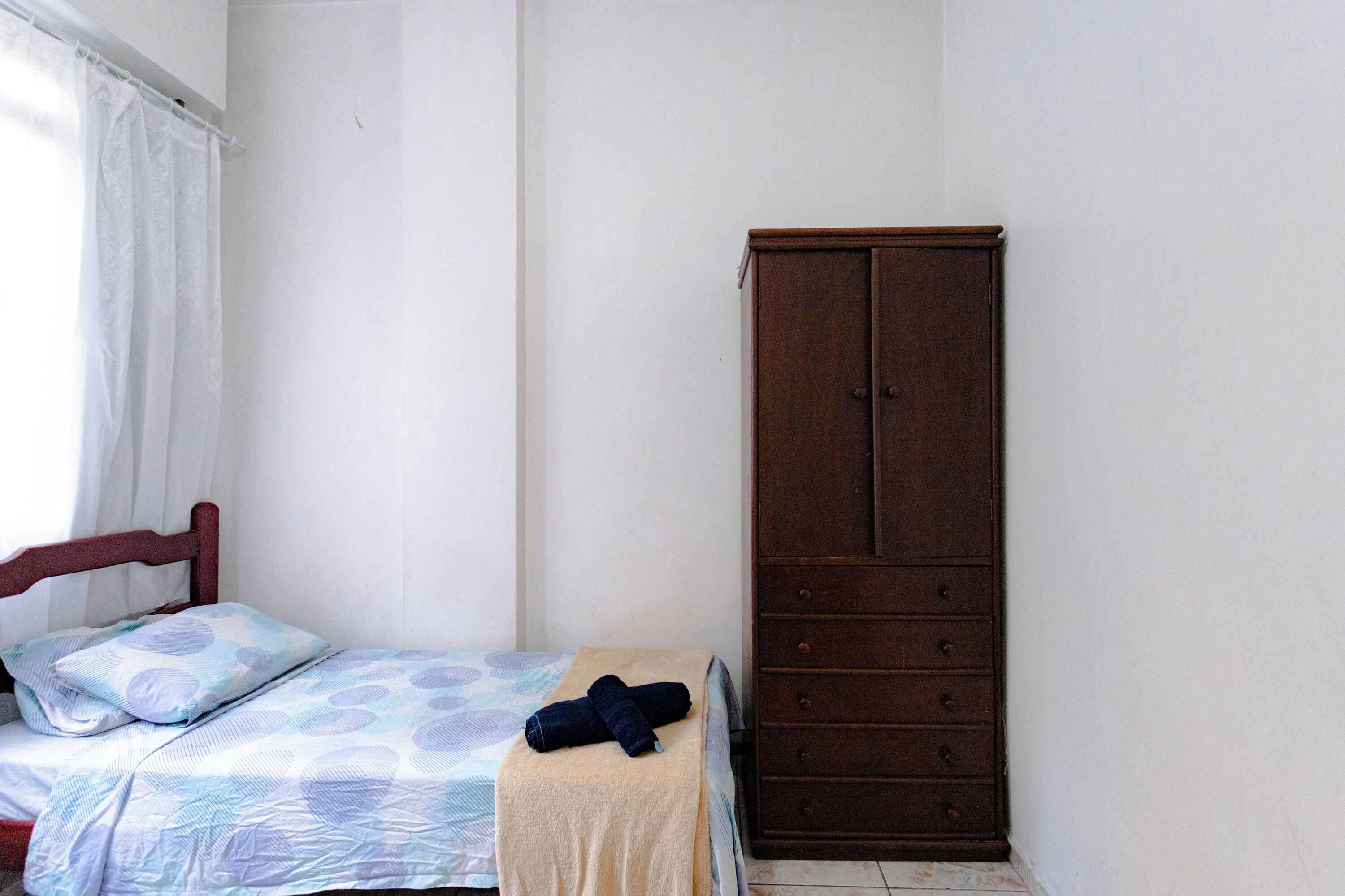 A bedroom with a bed, a wooden wardrobe, and a window with curtains.