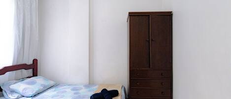 A bedroom with a bed, a wooden wardrobe, and a window with curtains.