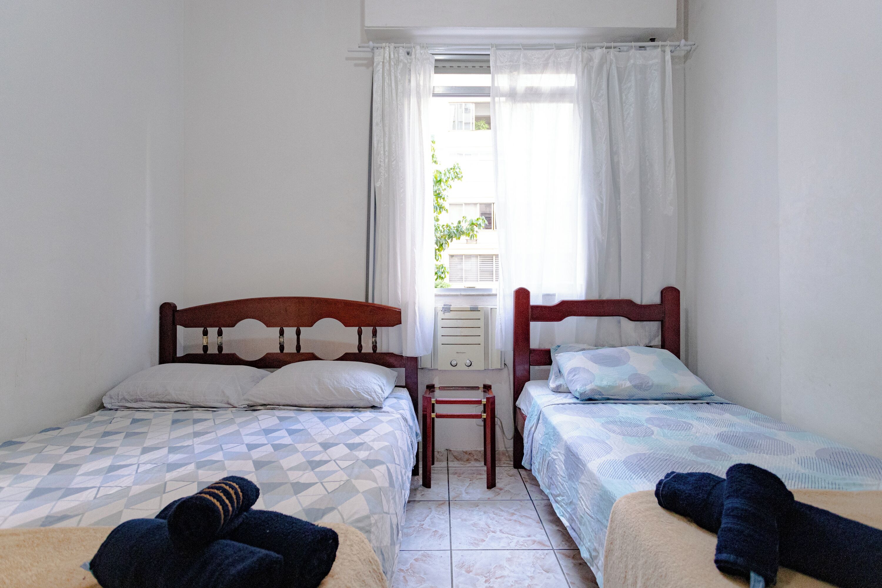 A room with two beds, a small table, and a window with curtains.