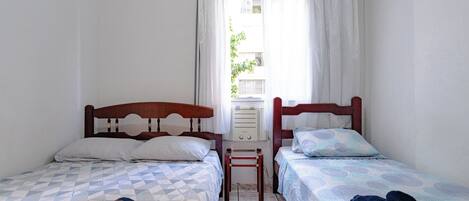 A room with two beds, a small table, and a window with curtains.