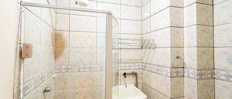 A bathroom with a glass-enclosed shower, a sink, and tiled walls.