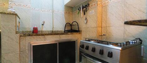 A kitchen with a gas stove, oven, and a microwave. There is a sink with a faucet and a cabinet above it.