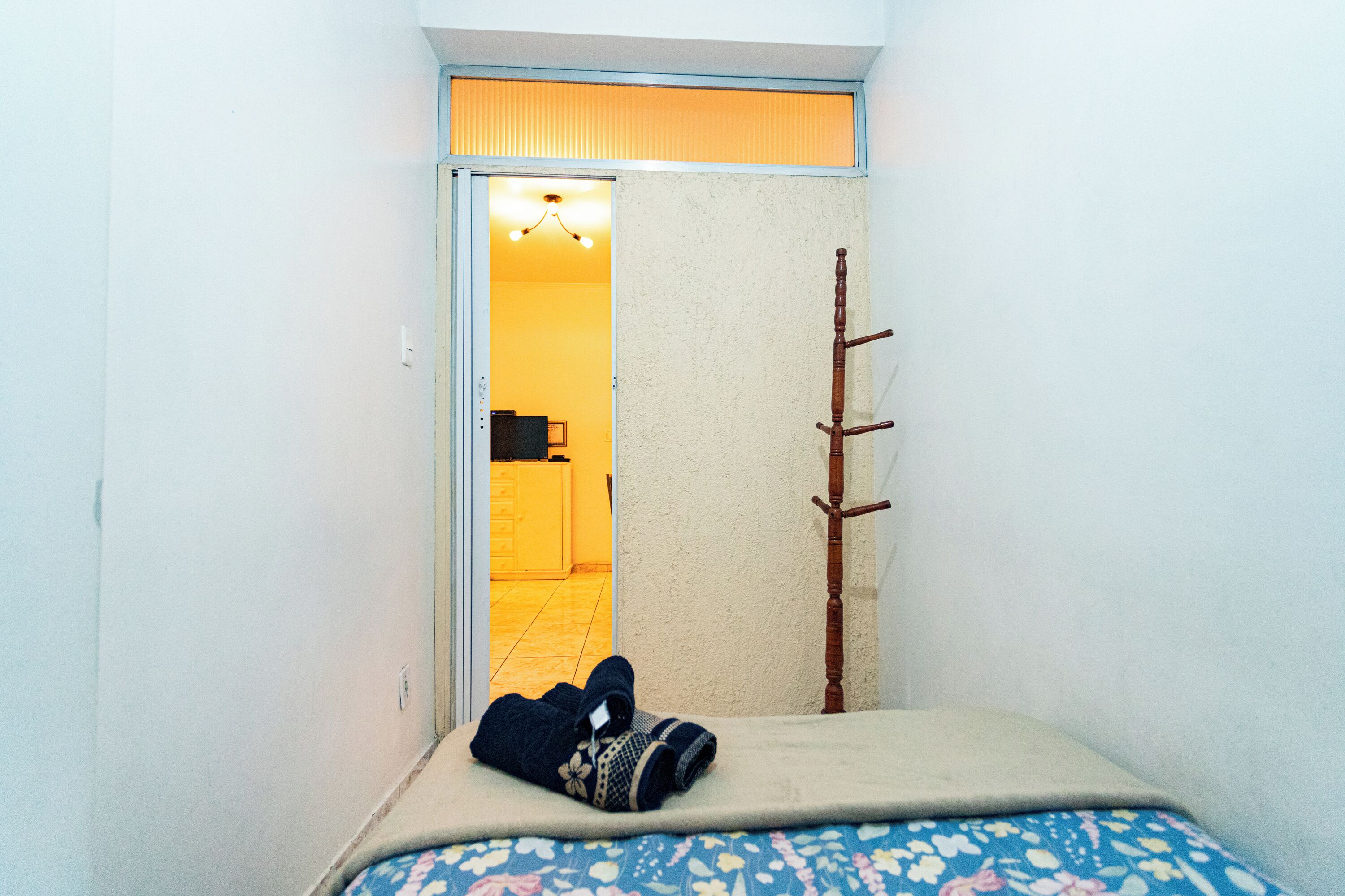Ein kleiner, schmaler Raum mit einem Bett, einer an der Wand lehnt Holzleiter und einer Tür zu einer Küchenzeile.