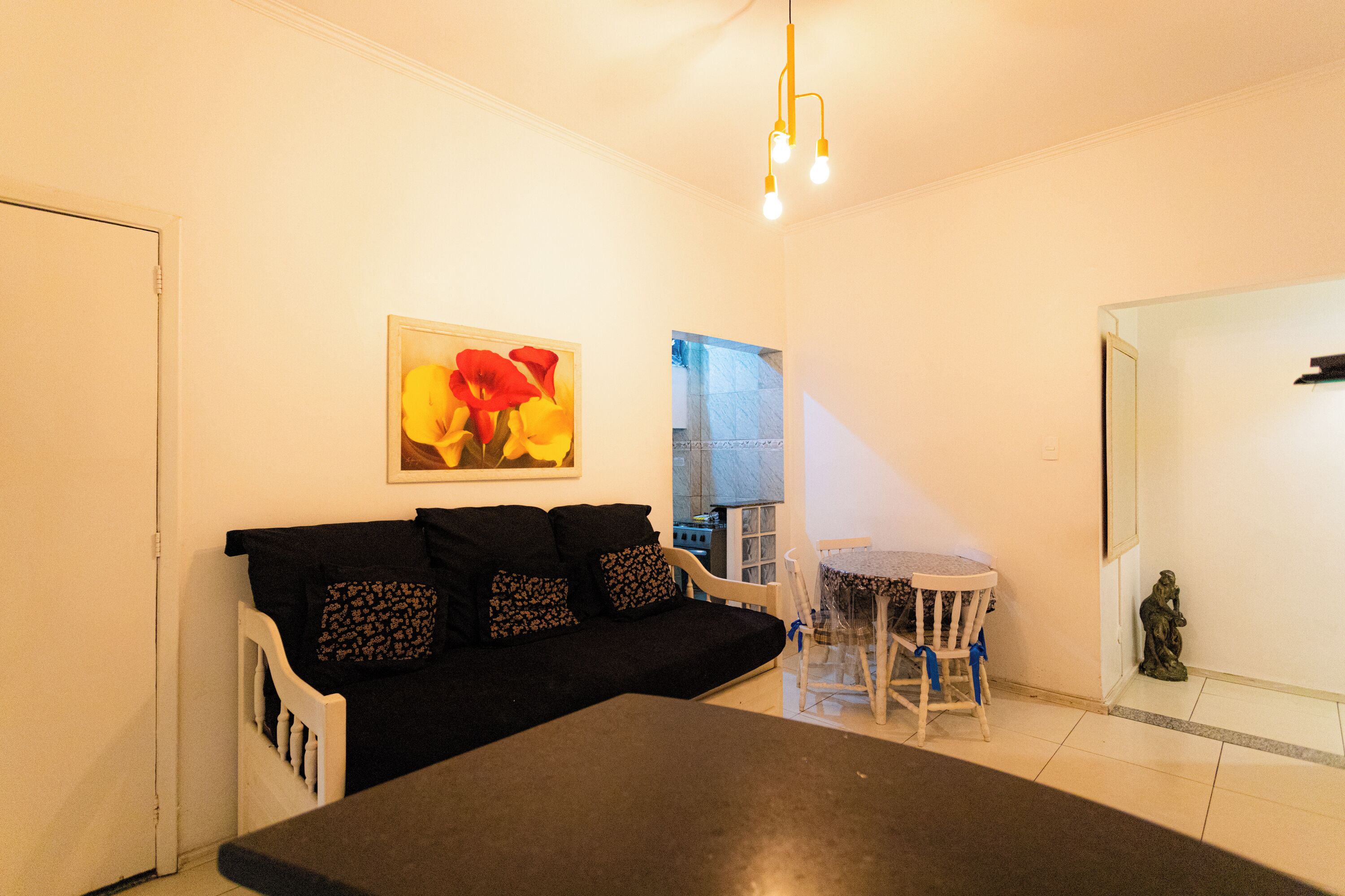 Uma sala de estar com um sofá preto, uma mesa de jantar e uma pequena estátua.
