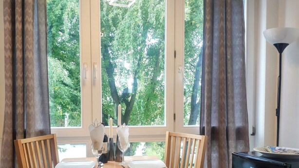 Spiseplads med et bord dækket til to personer, to træstole, et sort køleskab og en lampe.