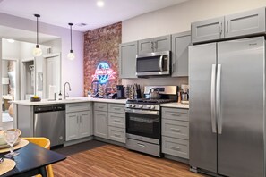 Enjoy cooking in this kitchen with a gas stove, microwave, and refrigerator, complemented by grey cabinetry and a brick accent wall.