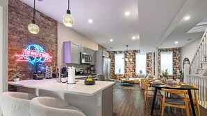 A modern kitchen with a neon sign, a dining area with a black table and yellow chairs, and a staircase leading to another level.
