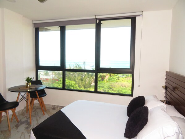 A bedroom with a bed, a window with a view, a small table with chairs, and a potted plant. - Takh703 (Cancún)