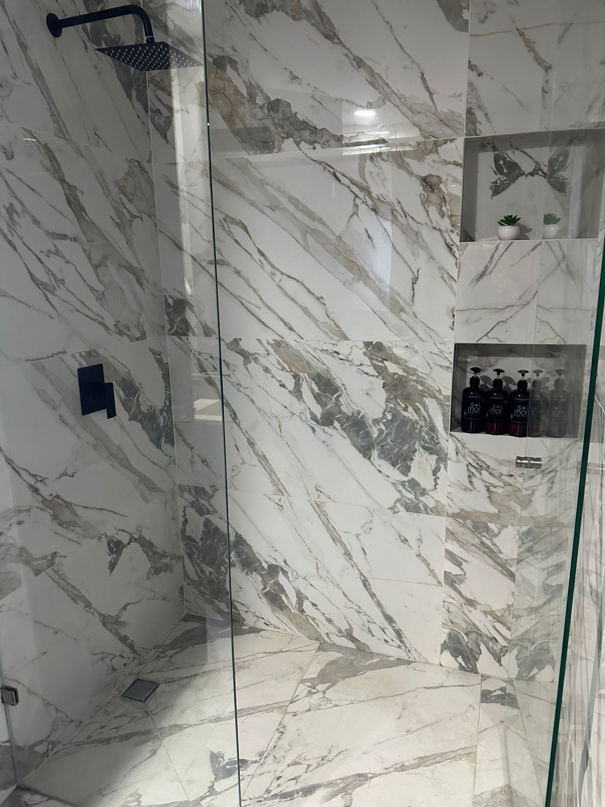 Eine Dusche mit Glastür, Marmorwänden und Ablage für Toilettenartikel.