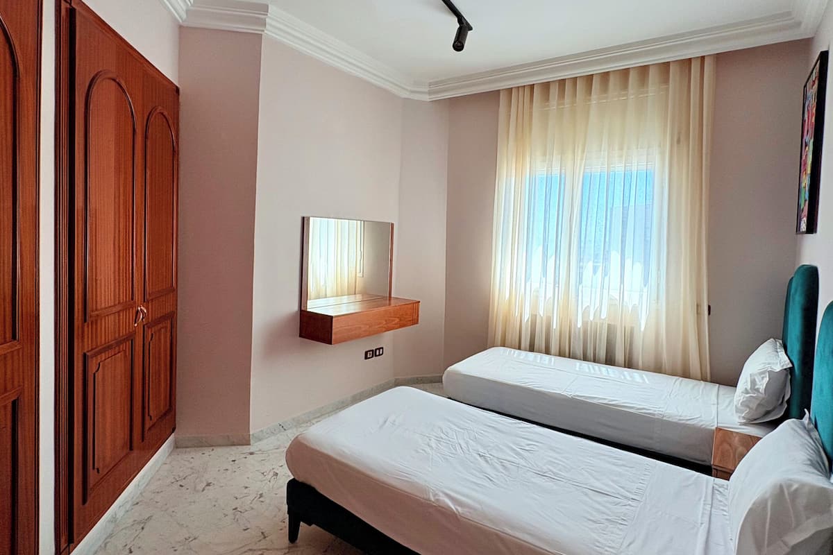 Een hotelkamer met twee bedden, een houten garderobe, een spiegel en een raam met gordijnen.