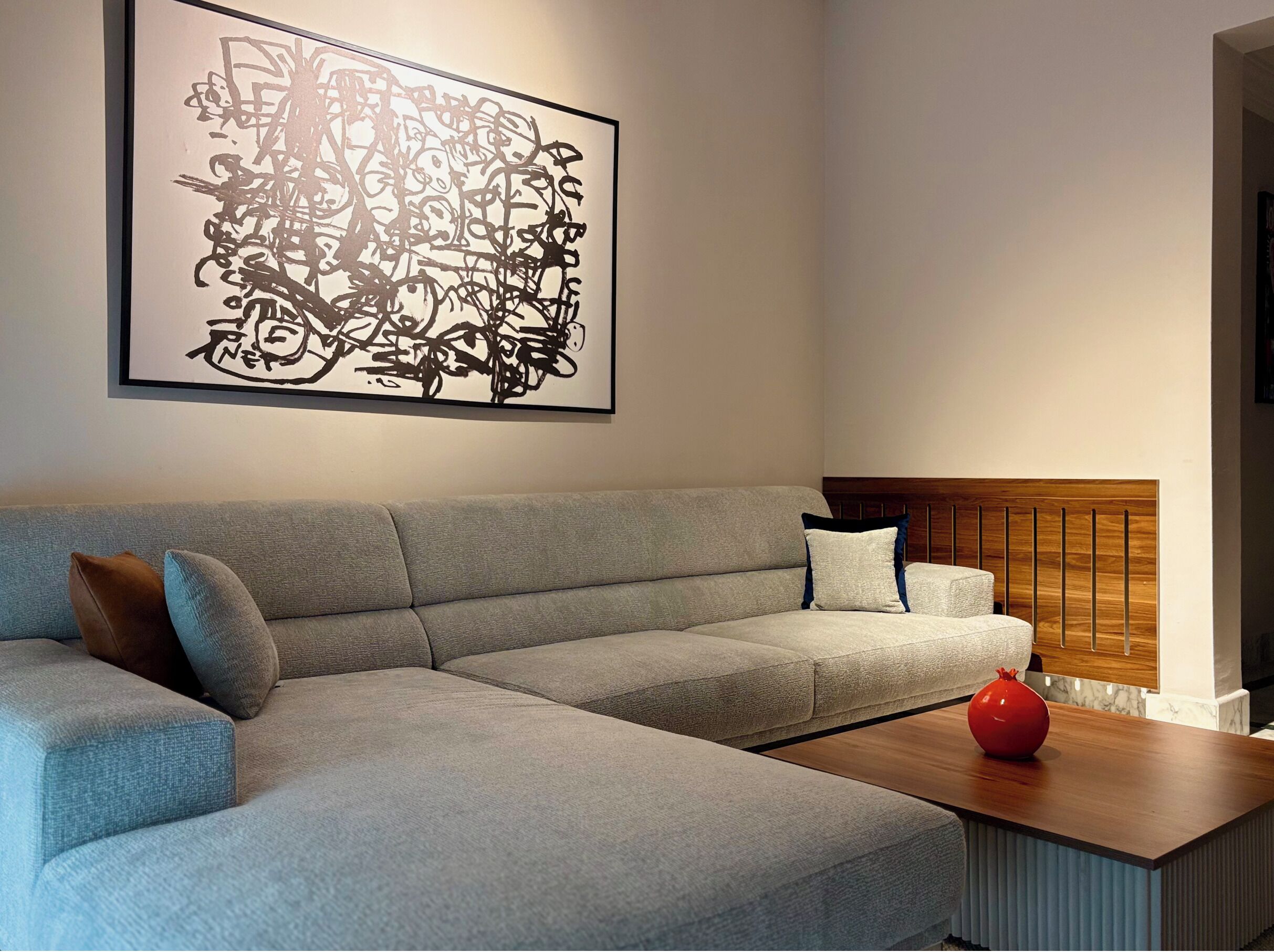 En moderne stue med en grå hjørnesofa, et træ sofabord og et stort abstrakt billede på væggen.