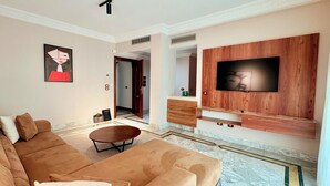 Una sala moderna con un sofá grande, una mesa de centro, un televisor de pantalla plana montado en una pared de madera y un pasillo que conduce a otra habitación.