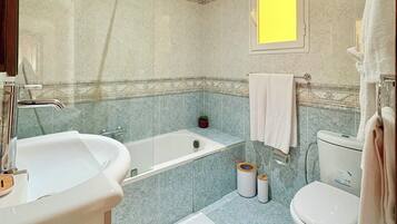 A bathroom with a bathtub, sink, toilet, and a small potted plant.