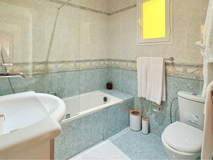 A bathroom with a bathtub, sink, toilet, and a small potted plant.
