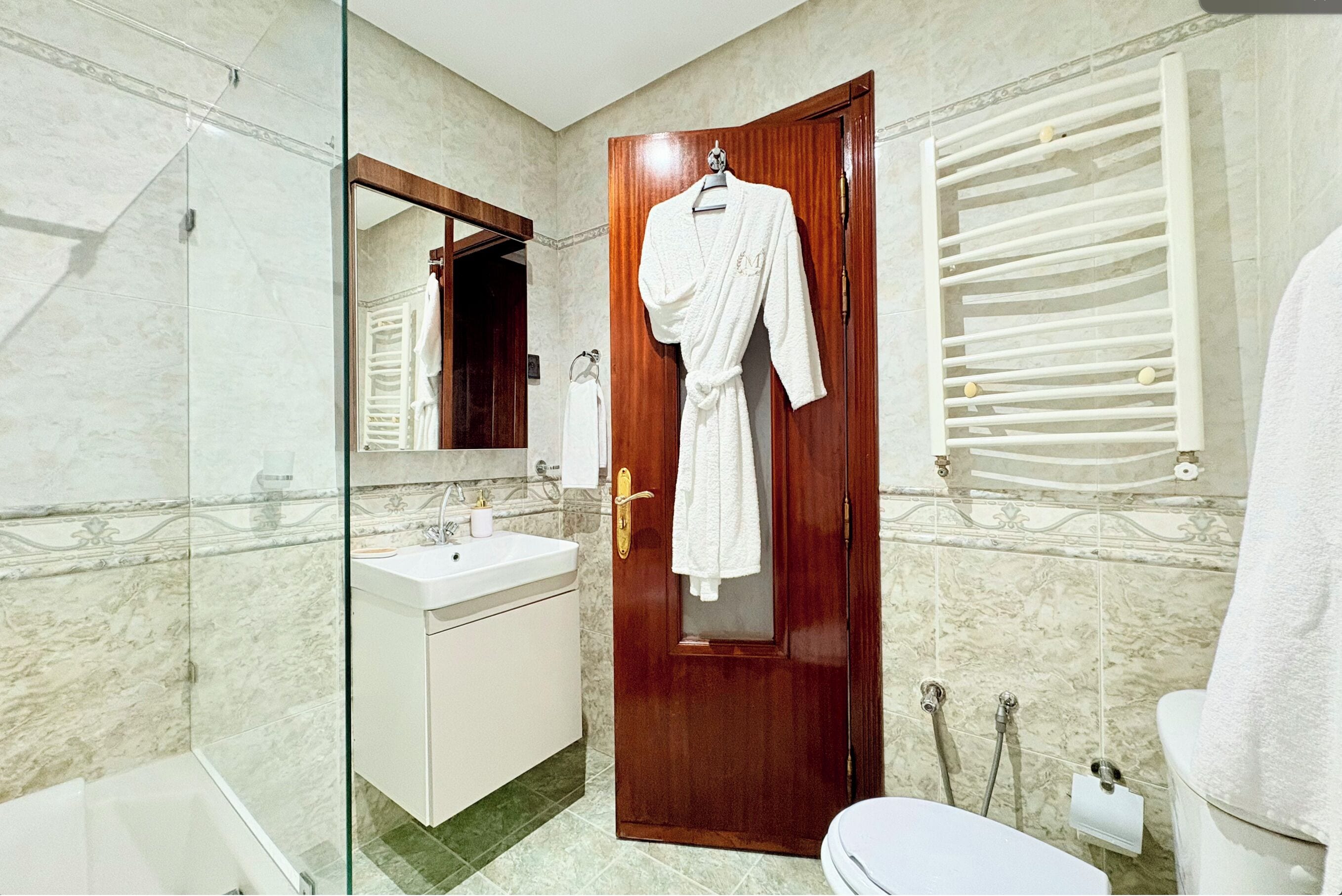A bathroom with a wooden door, a white sink, a glass shower enclosure, and a towel rack.