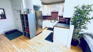 A modern kitchen with white cabinets, a stainless steel refrigerator, and a wooden floor.