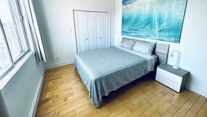 A bedroom with a bed, a nightstand, a window, and a painting on the wall.