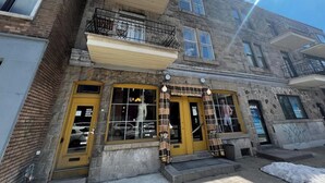 En bygning med flere etager, butik i stueetagen, synlig brandstige og en klar himmel.