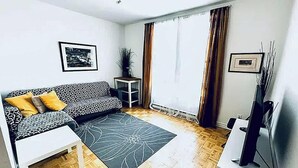 Una sala con un sofá estampado, una mesita auxiliar, una lámpara de pie y un ventanal con cortinas.