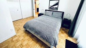Un dormitorio con cama, mesita de noche, un cuadro en la pared y una puerta.