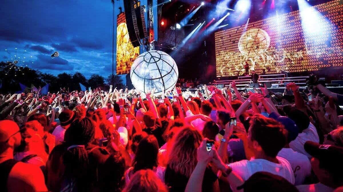 A crowded outdoor event with a stage and large screen.