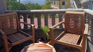 Een balkon met twee houten stoelen en een kleine tafel, met uitzicht op een schilderachtig zeegezicht en gebouwen.