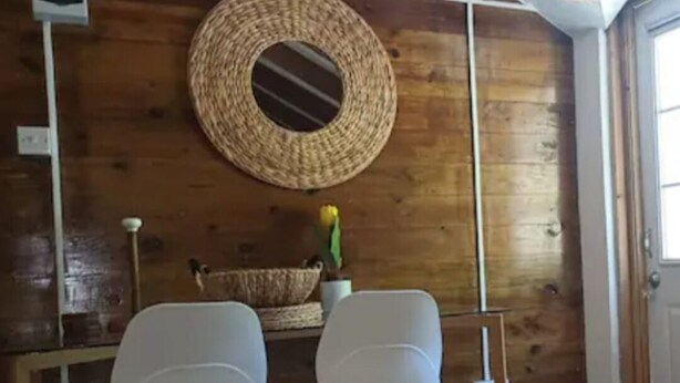 Een kamer met houten wanden, een geweven mand aan de wand en twee witte stoelen met houten poten.