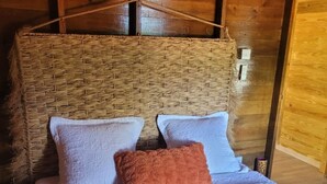 Een gezellig bed met een geweven hoofdbord, twee kussens en een gebreid plaid in een kamer met houten wanden.