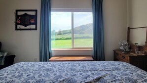 A bedroom with a bed, a window with curtains, a bedside table, and a wall-mounted picture. - 8 Mile Farm B&B (The Dalles)