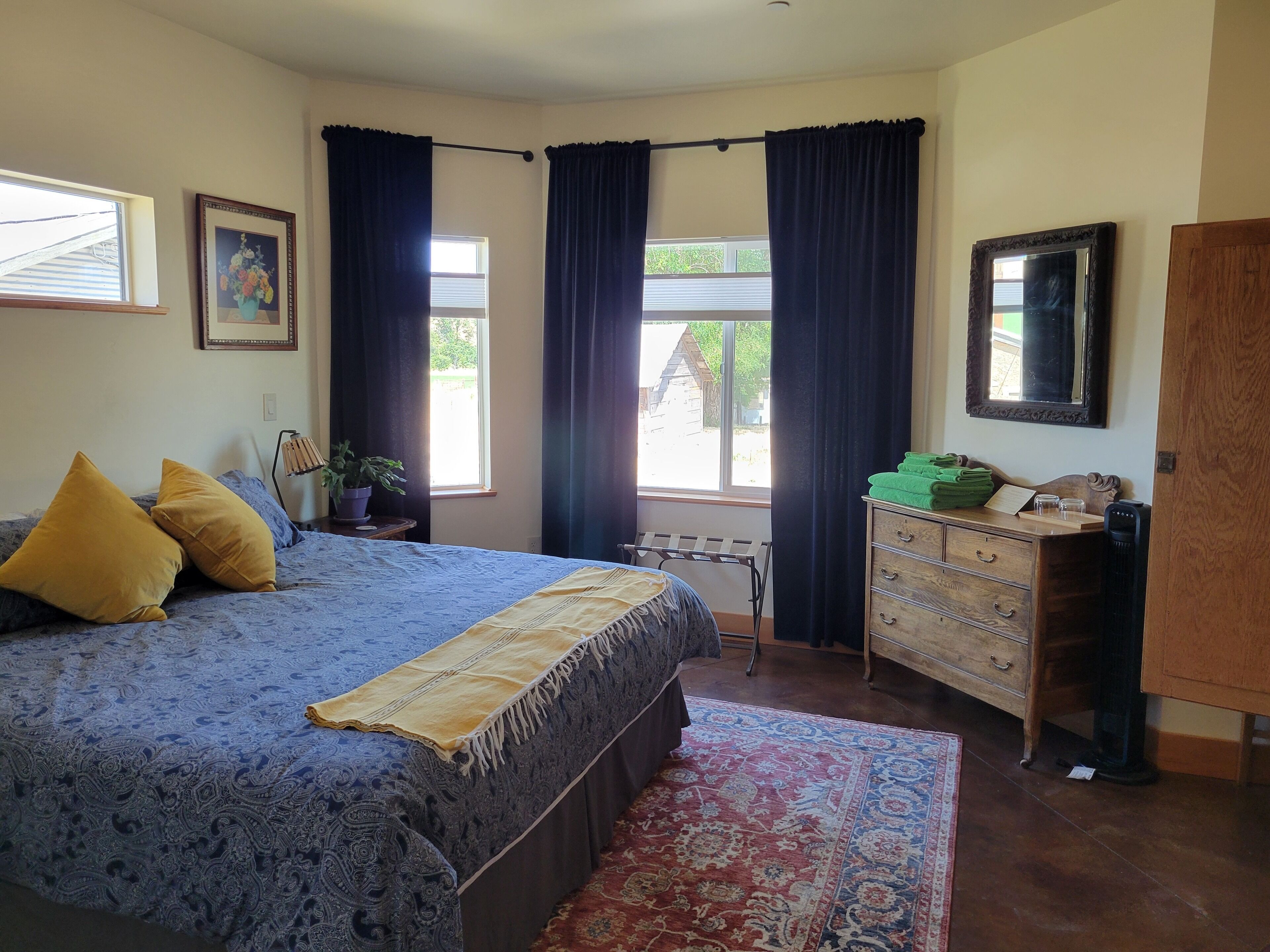 A bedroom with a bed, a dresser, a mirror, and a window with curtains.