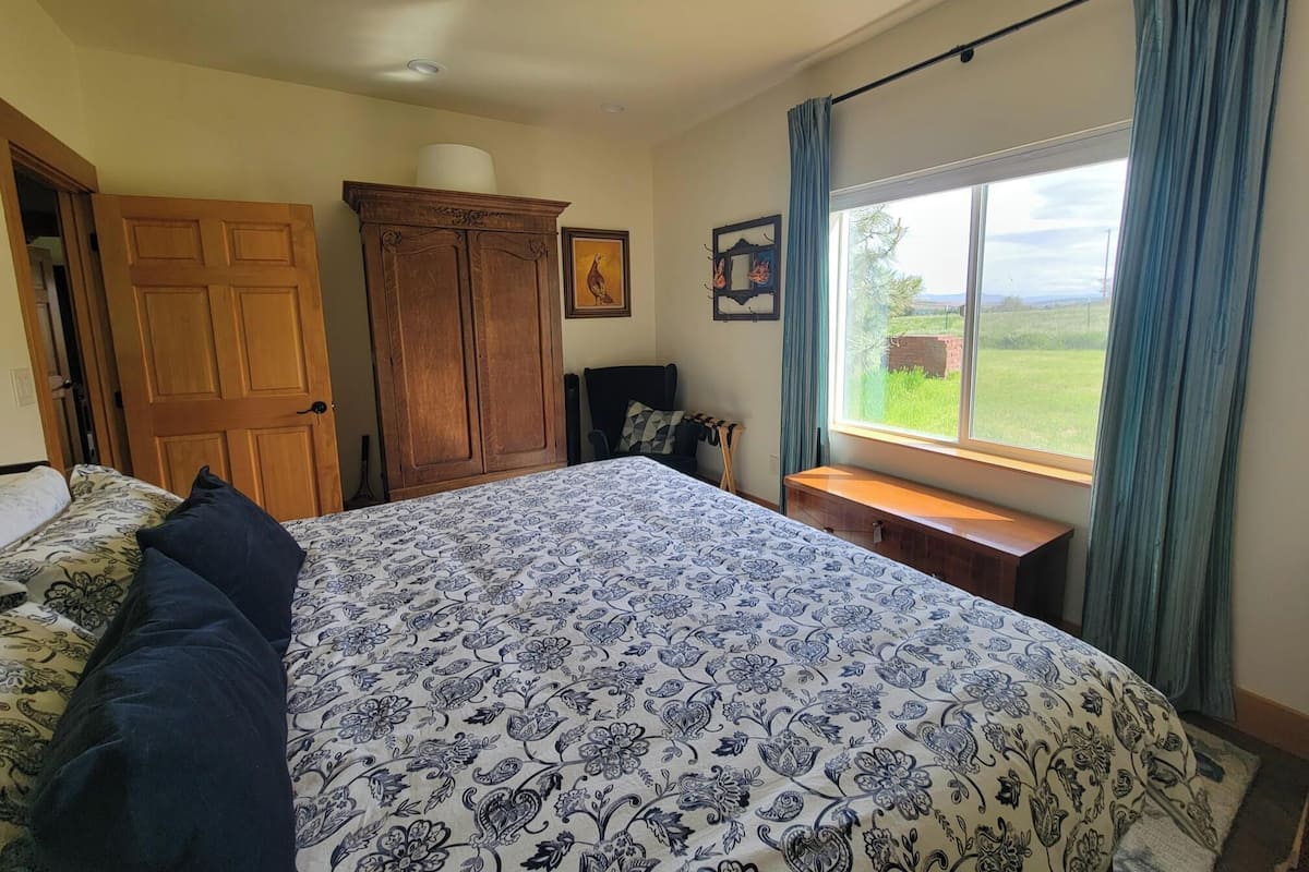 Un dormitorio con una cama grande, un armario de madera, un banco junto a la ventana y vistas al exterior.