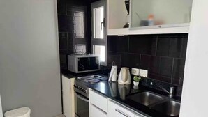 A compact kitchen with a microwave, stove, sink, and white cabinets. - 2 rooms apartment w/ garage included in Palermo (Buenos Aires)