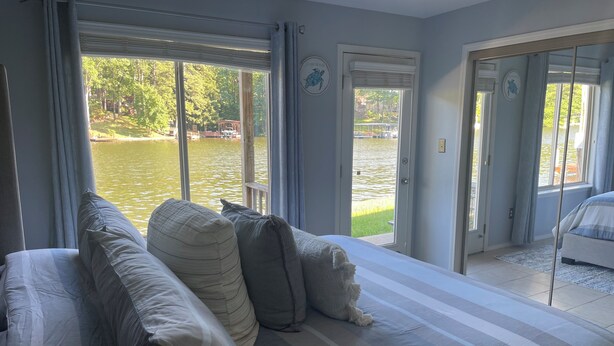A bedroom with a large bed, a view of a lake, and a door leading to another room.
