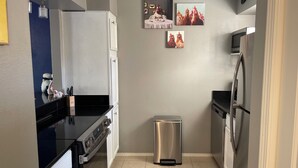 A compact kitchen with a black countertop, stainless steel appliances, and a trash bin.