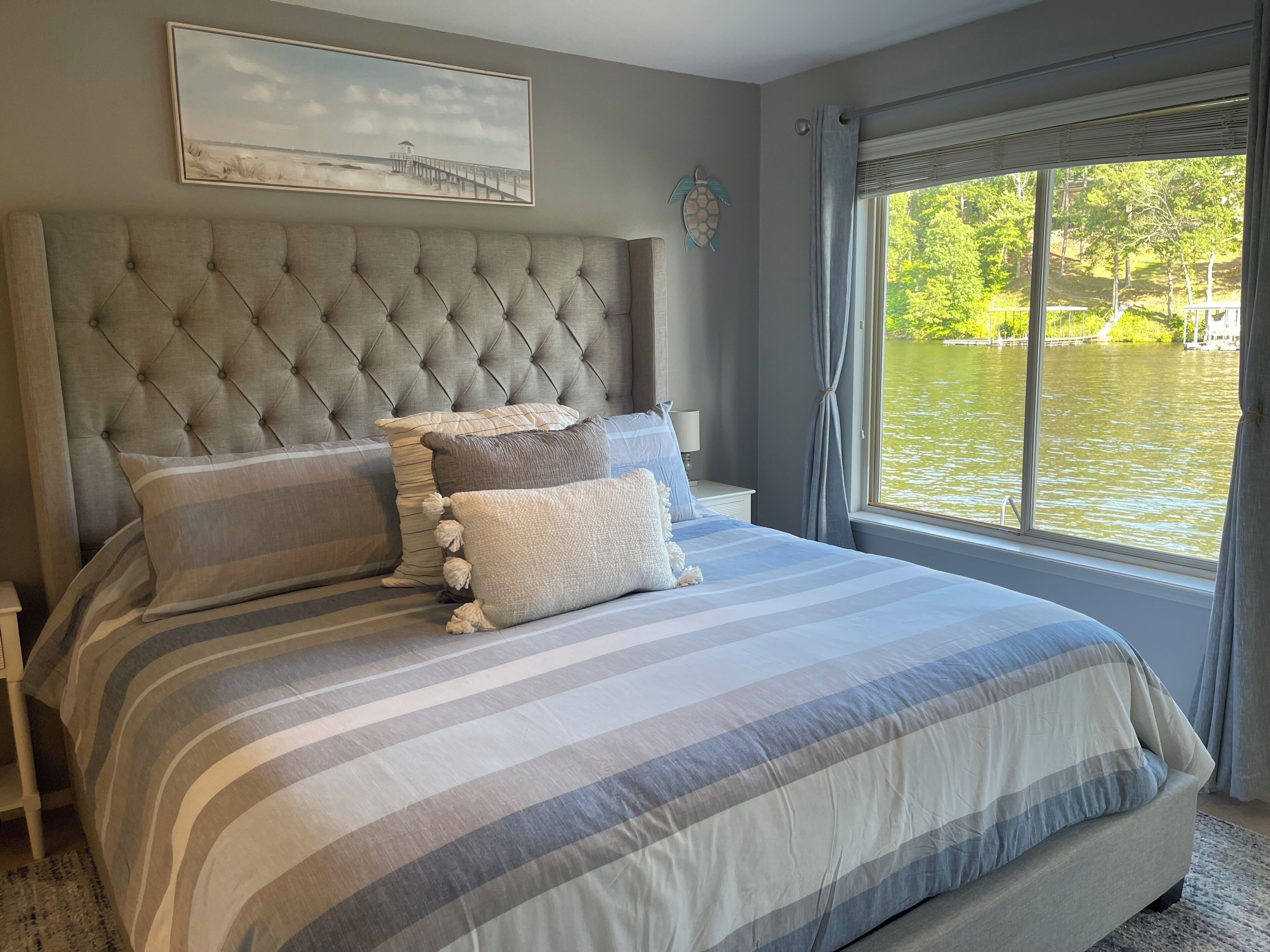 Una camera da letto con un letto grande, una testiera trapuntata e vista su un lago attraverso una finestra.