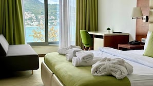 A hotel room with a bed, a desk, a chair, and a view of a mountainous landscape. - Porto Sole Hotel (Sutomore)