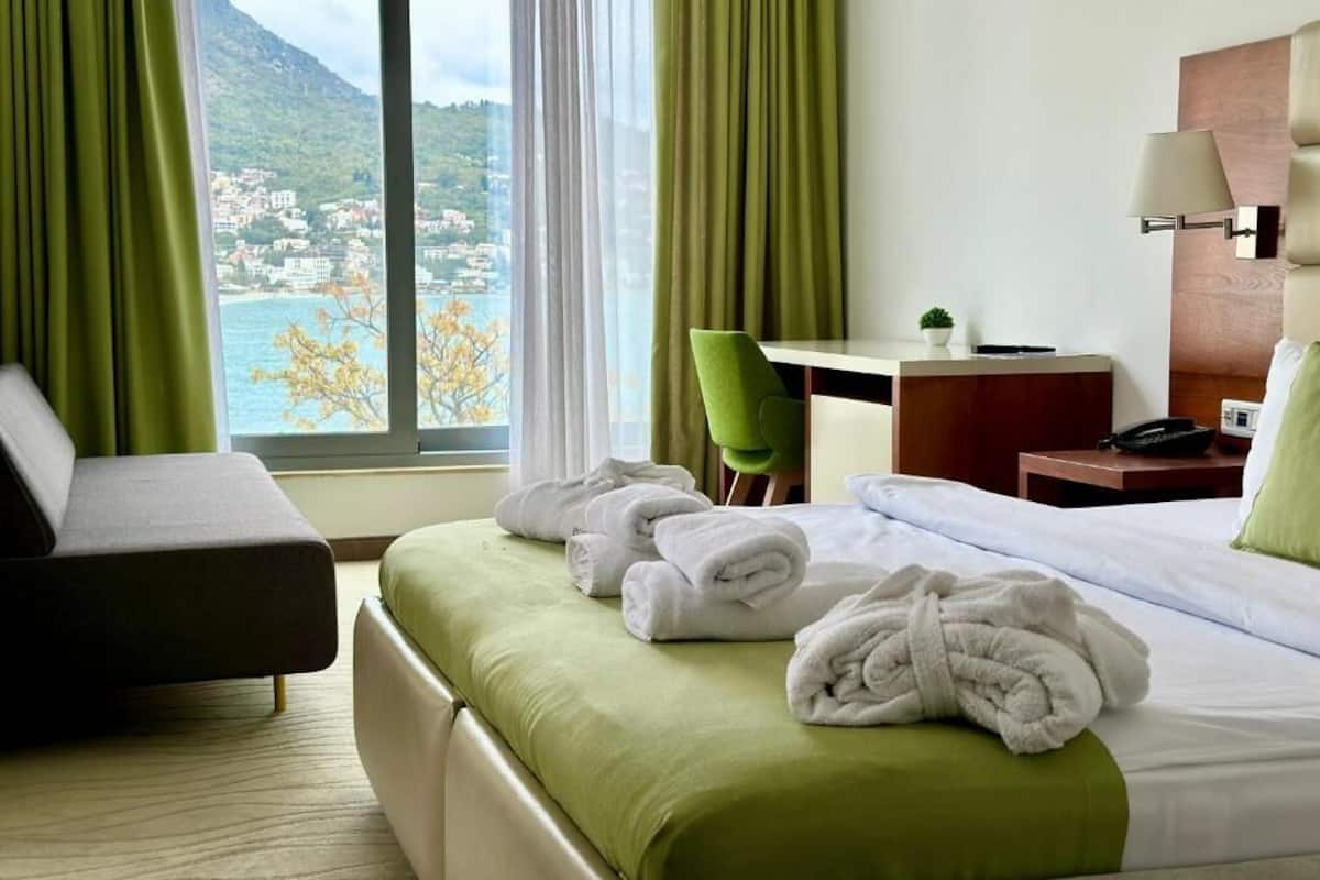 A hotel room with a bed, a desk, a chair, and a view of a mountainous landscape.