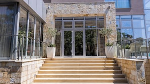 A hotel entrance with stone steps, large glass doors, and potted plants. - Porto Sole Hotel (Sutomore)