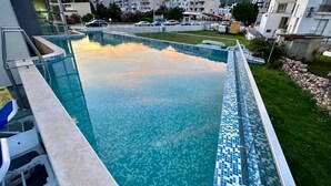 A swimming pool with a tiled edge, surrounded by a grassy area and buildings in the background. - Porto Sole Hotel (Sutomore)