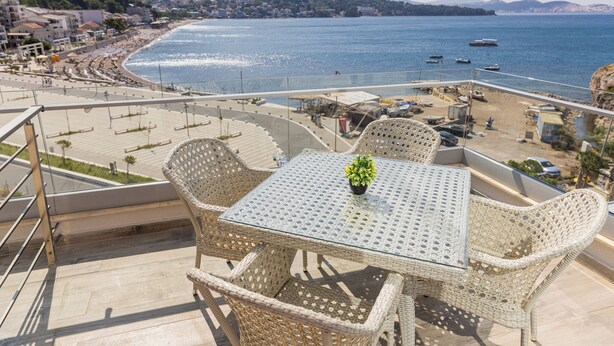 A balcony with wicker furniture and a glass table, overlooking a beach and the sea. - Porto Sole Hotel (Sutomore)
