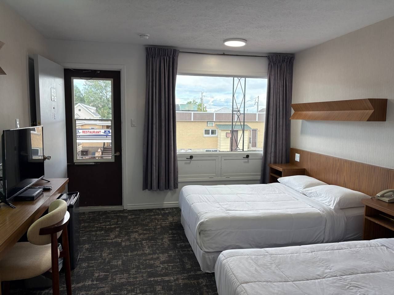 A hotel room with two beds, a desk with a chair, a television, and a window with curtains.