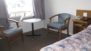 Camera d'albergo con un letto, due sedie, un tavolino rotondo, un comodino con un telefono e una finestra con tende.