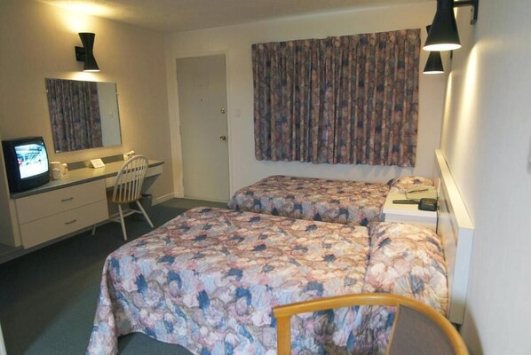 A room with two beds, a desk, a chair, a television, and a door.
