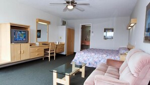 Una camera d'albergo con un letto, una scrivania, una sedia, un divano, una televisione, una ventola a soffitto e uno specchio.