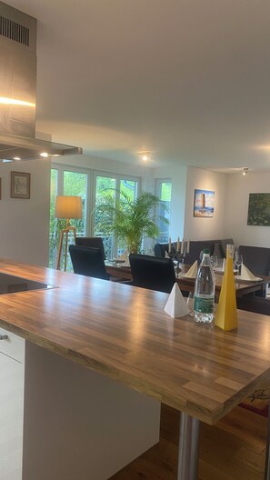 A modern kitchen with a wooden countertop, a dining area with a table set for two, and a large window with a view of greenery. - Modern 5-bedroom house on the Tuniberg in Fribourg (Freiburg im Breisgau)