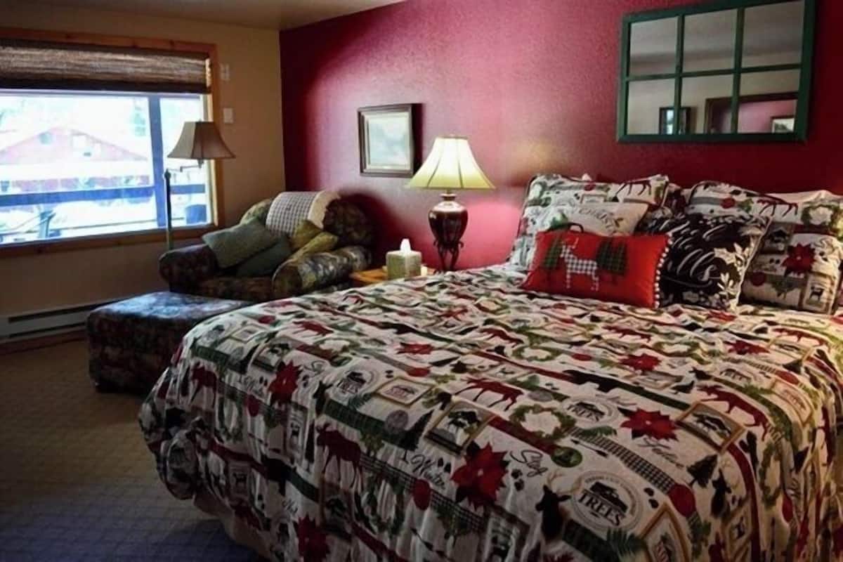 Un dormitorio con una cama grande, una ventana con persianas, una lámpara de noche y un espejo en la pared.