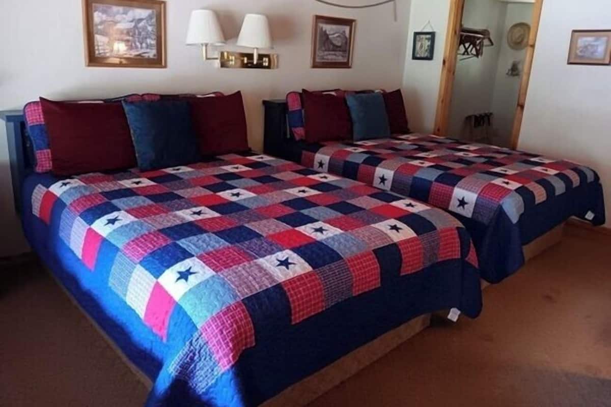 Habitación con dos camas, cada una cubierta con colcha de diseño de estrellas. Hay lámparas de pared y cuadros enmarcados en las paredes.