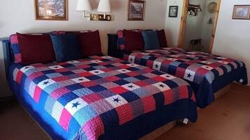 A room with two beds, each covered with a quilt featuring a star pattern. There are wall-mounted lamps and framed pictures on the walls.