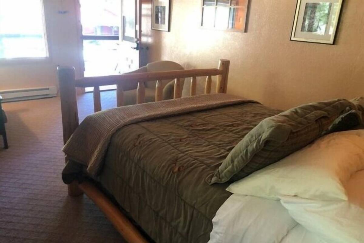 Un dormitorio con estructura de cama de madera, colcha marrón y almohada blanca.