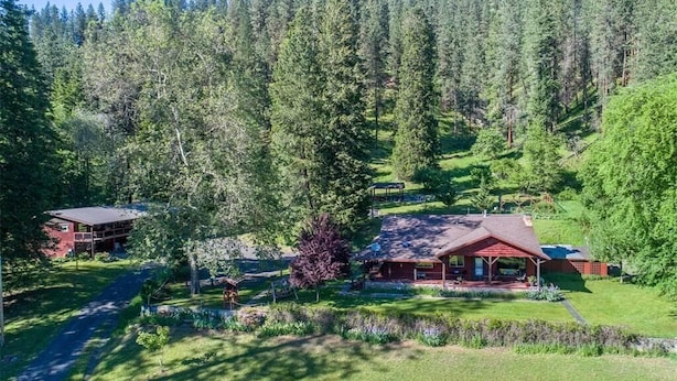 A lodge with two main buildings, surrounded by dense forest and a well-maintained lawn. - Reflections Inn (Kooskia)